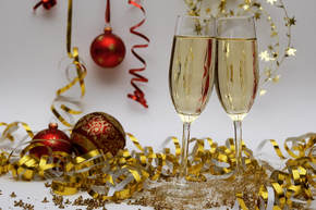 Picture of filled two champagne flutes, read and gold streamers and Christmas baubles.
